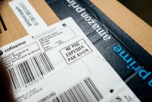 Paris, France - Dec 19, 2024: Close-up of an Amazon Prime cardboard package featuring a Colissimo shipping label from Spain to France with a warning sign in French stating Do Not Ship by Plane