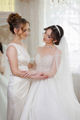 Two women are standing next to each other, one of them is wearing a wedding dress. The other woman...