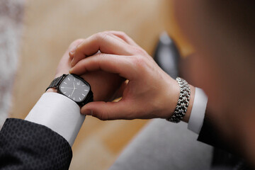 A man is wearing a watch and looking at it. The watch is black and has a square face