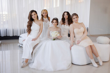 A group of women are sitting on a couch, one of them is wearing a white dress and holding a bouquet