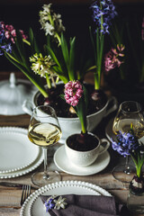 Spring elegant wedding or Easter celebration table decor. Festive white china, floral decoration with blooming bulbous hyacinth. Dark background. Springtime home gardening