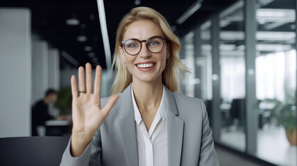 A businesswoman smiling while waving at the camera from an office setting. 