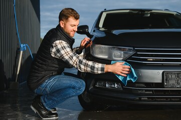 A man wipes his car with a microfiber towel after washing it at a car wash