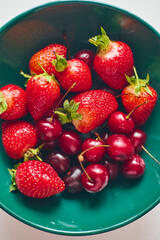 Strawberries and sweet cherries in a green plate, close-up