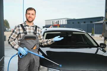 Portrait of a car wash station worker holding a water jet gun next to a clean car