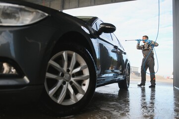 A car wash worker is using high pressure water gun for car washing