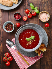 Thick rich Tomato puree Soup garnished with basil leaves and spices in bowl with Grilled Croutons on dark wooden table