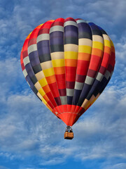 Fototapeta premium Looking up from below at a colorful hot air balloon flying in a sky with thin wispy white clouds.