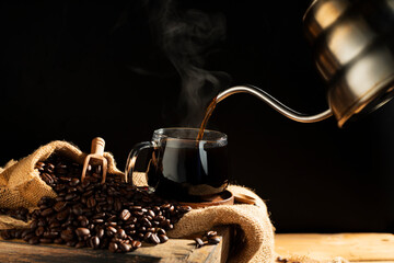 Pour black coffee into a coffee cup There are roasted coffee beans on the table. with a black background and dark colors