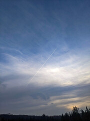 A contrail left by an aircraft streaking across the tranquil azure sky with cirrus clouds. Captures movement and serenity in an expansive atmospheric scene.