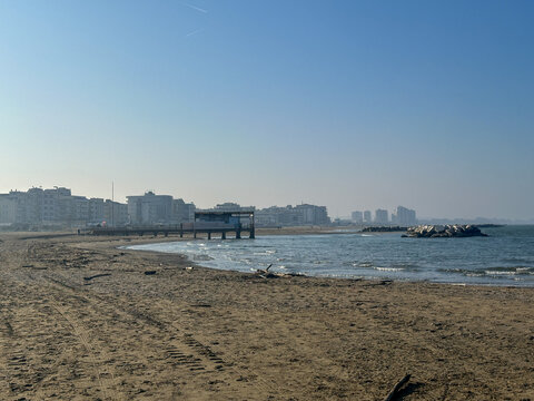 Wide, empty beach in Misano Adriatico, Rimini during winter. Clear sky above the sandy shore with distant buildings and the calm sea.
