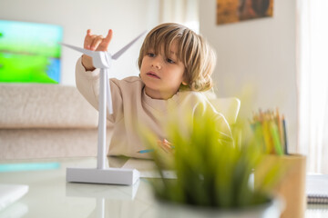 Preschooler interacts with a miniature wind turbine model at home, exploring renewable energy...