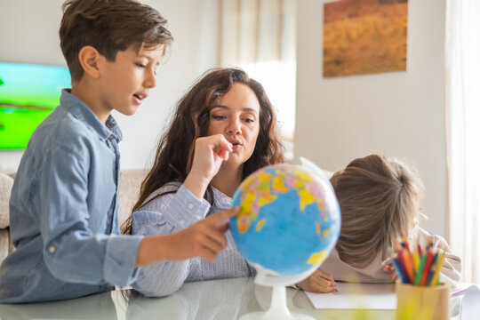 Mother pointing at globe teaching geography to her children during homeschooling, promoting education and family time in a comfortable home setting