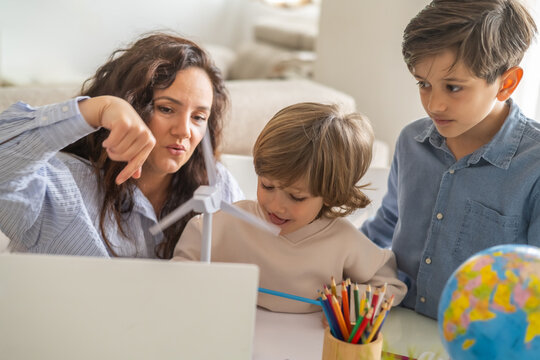 Mother pointing at a small wind turbine model, explaining renewable energy concepts to her two sons during a homeschooling session, focusing on stem education and sustainability - Powered by Adobe