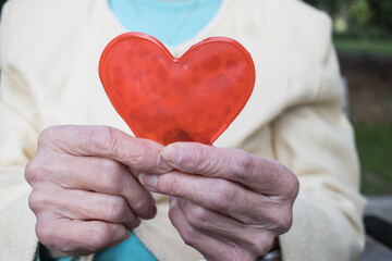senior woman hand caring for a heart, cardiology,  illness. Horizontal. Faceless.	
