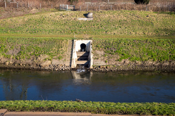 Drainage pipe discharging water into river surrounded by grassy banks