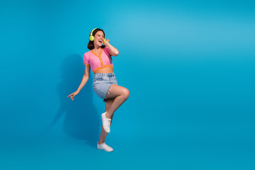 Young woman dancing and smiling in stylish summer clothing on a vibrant blue background