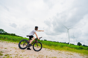 Naklejka premium Cyclist stopping to admire wind turbines in a green landscape on a cloudy day