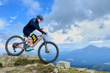 Fototapeta premium Cyclist man riding electric mountain bike outdoors. Male tourist biking along grassy trail in the mountains, wearing helmet. Concept of sport, active leisure and nature.