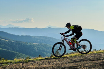 Cyclist man riding electric mountain bike outdoors. Male tourist biking along grassy trail in the...
