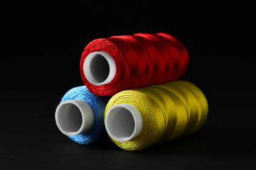 Spools of colorful sewing threads on black background, closeup