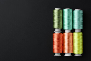 Spools of colorful sewing threads on black background, flat lay. Space for text