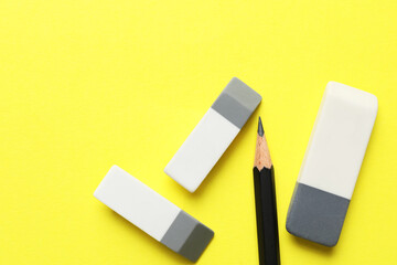 Erasers and pencil on yellow background, flat lay. Space for text