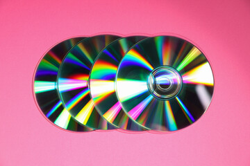 Many shiny compact discs on pink background, top view