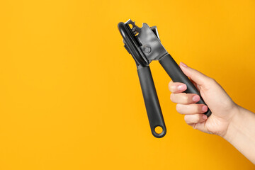 Woman holding can opener against yellow background, closeup. Space for text