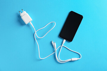 Triple charge cable connected to smartphone on light blue background, top view