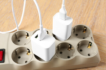 USB adapters with charge cables in power strip on wooden table, closeup