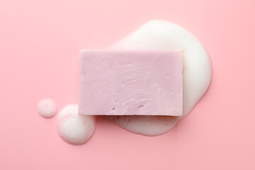 Soap bar with foam on light pink background, top view