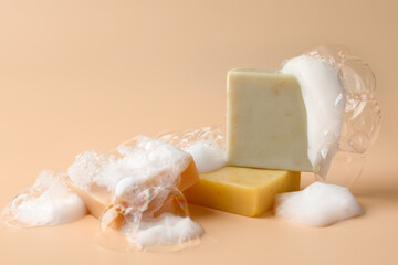 Soap bars with foam on beige background, closeup. Space for text