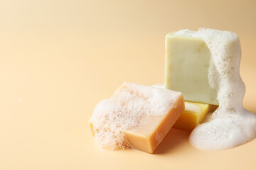 Soap bars with foam on beige background, closeup. Space for text