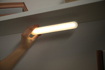 Woman putting modern LED lamp onto shelf indoors, closeup
