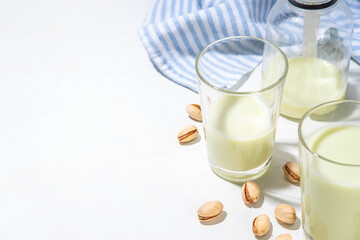 Vegan alternative Pistachio Milk,  Healthy vegetarian drink. Two glass with non-dairy milk beverage, on white kitchen table with pistachio nuts, copy space