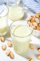 Vegan alternative Pistachio Milk,  Healthy vegetarian drink. Two glass with non-dairy milk beverage, on white kitchen table with pistachio nuts, copy space