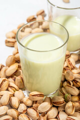 Vegan alternative Pistachio Milk,  Healthy vegetarian drink. Two glass with non-dairy milk beverage, on white kitchen table with pistachio nuts, copy space