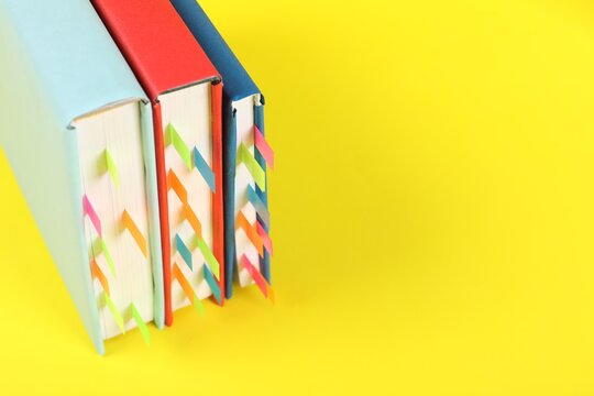 Books with colorful tabs on yellow background, closeup. Space for text