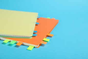 Notebooks with colorful tabs on light blue background, closeup. Space for text