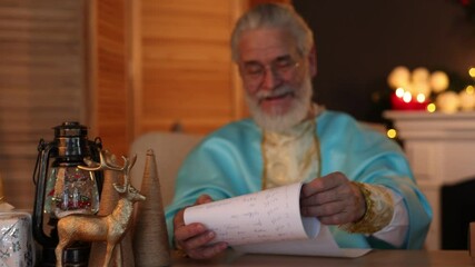 Saint Nicholas reading wish list in room decorated for Christmas. Camera moving right