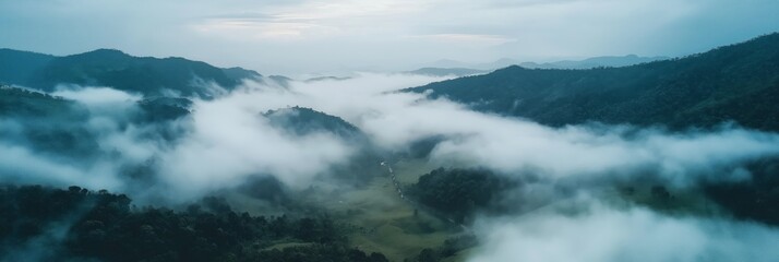 Naklejka premium Bird eye view captures a panoramic landscape of a mountain valley shrouded in low-lying clouds with a distant horizon under a soft, overcast sky