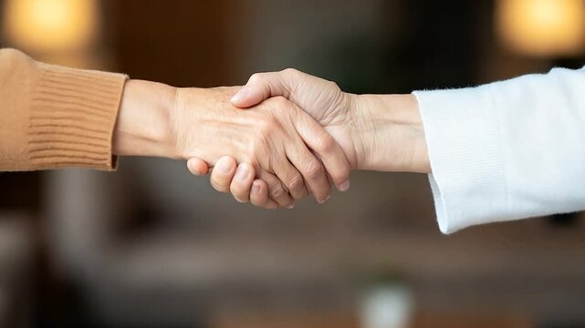 Two individuals shaking hands in a warm, inviting indoor setting with soft lighting
