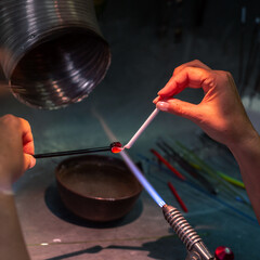Glass bead making with torch flame in artisan workshop. 