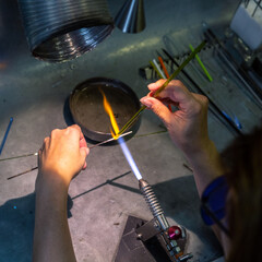 Glass artist shaping molten glass with torch flame. 