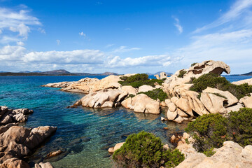 A scenic view of the rocky coastline of Sardinia, Italy, with crystal-clear turquoise water and lush green vegetation. Mediterranean holiday destination.