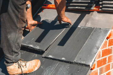 Skilled worker laying black slate tiles on a building roof, showcasing craftsmanship and focus on...