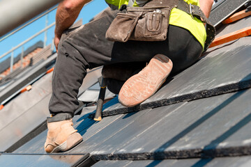 Roofer installing tiles on a steep roof © Iryna