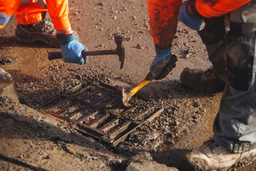 Workers cleaning road gully clogged with mud