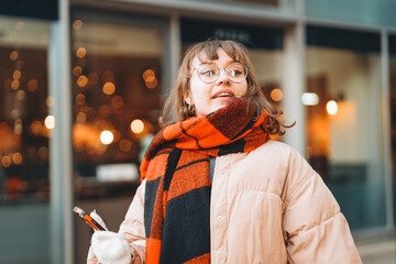 Young woman enjoying winter day in city, wearing puffy coat and  vibrant plaid scarf while holding...